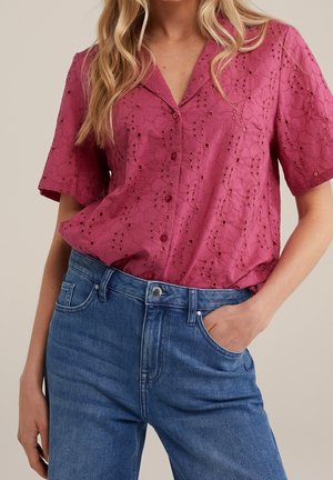 Camicia rosa a maniche corte con bottoni, con ricami floreali in rilievo, abbinata a jeans in denim blu a vita alta.