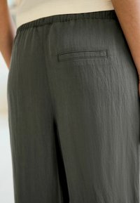 Pantaloni grigi scuri realizzati in tessuto leggero, con una texture liscia, vita elastica e una tasca posteriore con un semplice design a punto. 