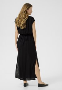 Black maxi dress with short sleeves, elastic waist, and side slits. Made from lightweight fabric, featuring a flowing design and soft texture.