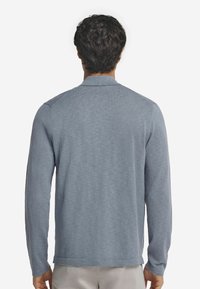 Långärmad, ljusblå stickad polotröja med krage och en avslappnad passform. Har en strävt yta och diskret ribbad detalj vid ärmsluten.