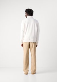 White sweatshirt with a high collar and ribbed hem, paired with beige loose-fitting trousers and light-colored shoes. Plain texture overall.