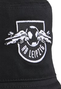 Casquette noire avec un logo brodé représentant un ballon de football et deux voitures volantes, texte "RB Leipzig" en dessous de l'emblème, design à visière plate.