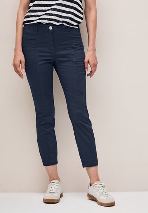 Pantalons en mélange de coton bleu marine avec une coupe slim, une longueur raccourcie, des poches avant et un devant plat, assortis à des baskets blanches.