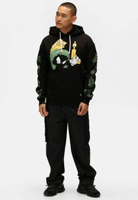 Felpa nera con grafiche di un personaggio dei cartoni in verde e giallo. Presenta polsini a costine e cappuccio con stringa. Abbinata a pantaloni cargo neri.