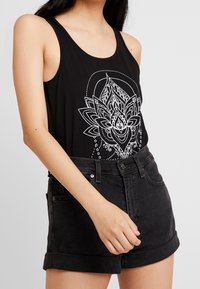 Débardeur noir avec un graphisme de fleur de lotus blanche, associé à un short en denim noir taille haute, présentant un ourlet roulé et une texture lisse.