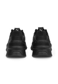 Paire de baskets noires Puma R-System vues de dos avec talons surélevés et tissu en mesh sur le dessus sur fond blanc.