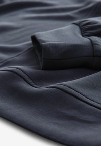 Navyblauwe stof, gladde textuur, toont een opgevouwen manchetten met elastische details; naden zijn zichtbaar, wat wijst op een aansluitend ontwerp.