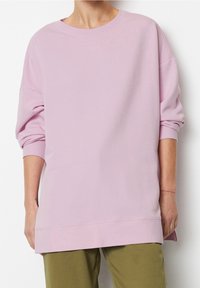 Sudadera oversized de color rosa claro con cuello redondo y hombros caídos, con puños acanalados y un dobladillo recto, combinada con pantalones de color verde oliva.