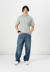 Grå kortærmet t-shirt parret med løse blå denimjeans. Hvite sneakers med gummisål. Enkel design, afslappet stil.