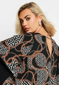Blusa nera con un audace motivo a catena multicolore e geometrico, dotata di una schiena con chiusura a chiave e sottili dettagli in oro.