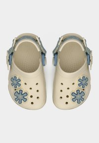 Sabots crème pour enfants avec décorations de fleurs bleues et sangles bleues ajustables, vus de dessus sur fond blanc.