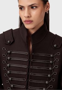 Chaqueta de estilo militar marrón hecha de lana, con acentos de botones, bucles decorativos y un cuello alto. Primer plano de los detalles del diseño.