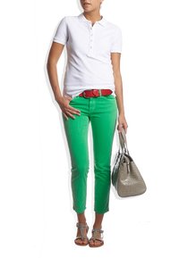 Camisa polo blanca, pantalones verdes ajustados, cinturón rojo, sandalias plateadas y un bolso gris texturizado con un patrón de cocodrilo.