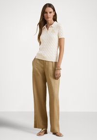 Stickad krämfärgad kortärmad pikétröja med flätmönster och gul logotyp; kombinerad med vidbenta linnebyxor i brunt och minimalistiska sandaler.