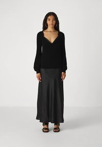 Fekete kötött hosszú ujjú felső V-nyakkivágással és pufi ujjak, hosszú, légies fekete selyemszoknyával párosítva. Simogató textúra és elegáns sziluett.