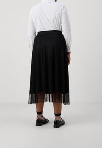 Fållad svart tyllkjol med svart midjeband, bärs med en vit långärmad skjorta. Svarta skor och strumpor med hjärt-mönster syns.