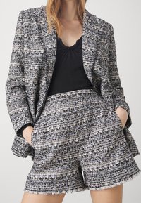 Completo blazer e pantaloni a pantalone corto in tessuto intrecciato testurizzato con tonalità blu, nero e crema. Presenta orlo frangiato e tasche evidenti.
