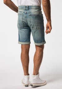 Shorts de mezclilla en un azul claro con dobladillos enrollados, con bolsillos traseros y una cintura alta, combinados con zapatillas altas blancas.