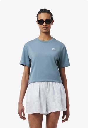 Blue cropped t-shirt in cotton with short sleeves and a crew neck, featuring a small white logo on the chest, paired with light striped shorts.