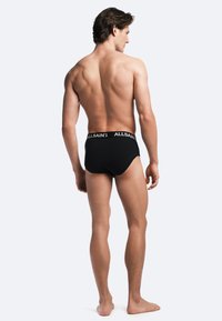 Black cotton brief with elastic waistband featuring white logo text, showcasing a snug fit and smooth texture, viewed from the back.