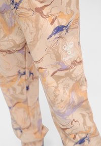 Marmorierte beige Hose mit blauen und braunen Akzenten, gefertigt aus einem weichen Material und mit einem weißen Hummel-Logo an der unteren Wade. Geeignet für aktive Bekleidung.