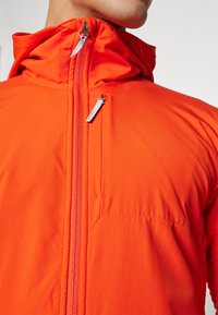 Bright orange jacket with a high collar, featuring a full front zipper and two zip pull tags. The fabric appears smooth and lightweight.