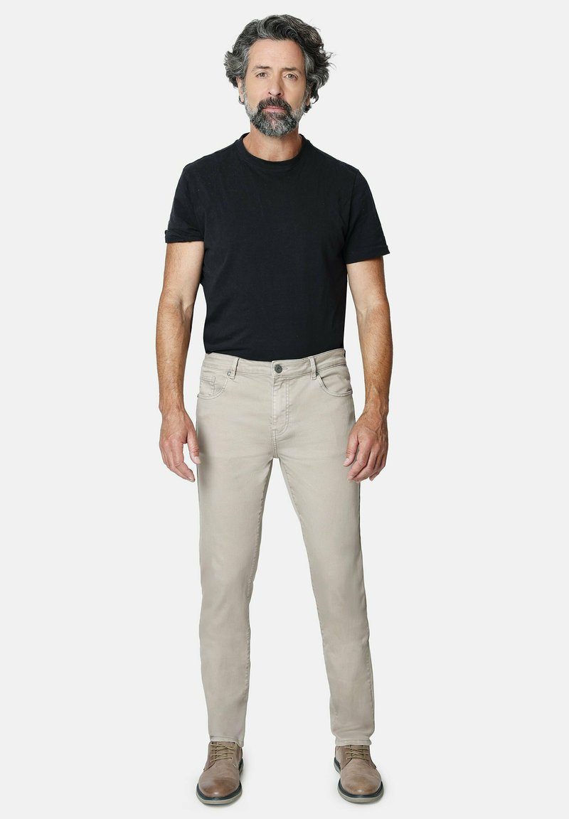 Pantalones de vestir de color beige claro con un ligero estiramiento, combinados con una camiseta negra de cuello redondo. El modelo lleva zapatos marrones con cordones.