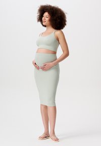Hellgrünes geripptes Umstandskleidungs-Set, bestehend aus einem taillierten Bralet und einem knielangen Rock, mit glatter Textur und schlichtem Design.
