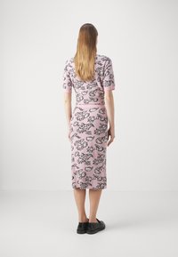 Gebreide, aansluitende jurk in lichtroze met zwarte bloemenpatronen. Korte mouwen en rok tot aan de knie. Gecombineerd met zwarte schoenen.