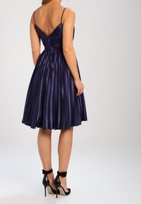 Námořnické skládání šaty s V-vyřezáváním na zádech, tenkými ramínky a přiléhavým korzetem. Nosené s černými lodičkami na kotníkovém popruhu. Hladký povrch látky.