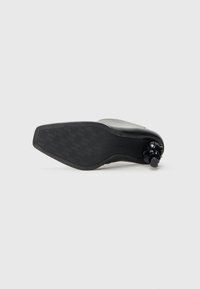 Black shoe sole with a smooth finish and houndstooth pattern. Features a circular accent near the heel. Sleek, low-profile design.