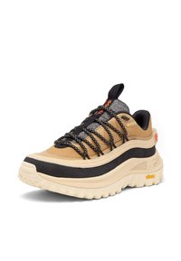 Baskets Gore-Tex beige et noires avec une épaisse semelle Vibram beige et des lacets noirs à motifs, inclinées vers la gauche sur fond blanc.