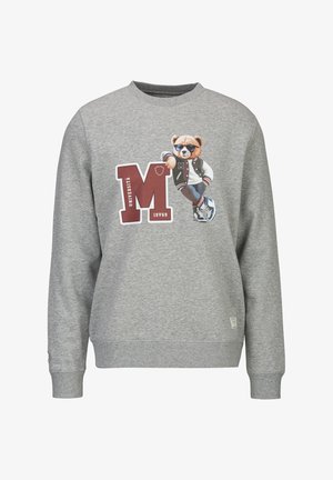 Grijze trui met een grote rode "M" en een teddybeer die een zonnebril, een varsityjack, een spijkerbroek en sneakers draagt en leunt tegen de letter.