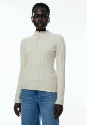 Crème-kleurige gebreide trui met een hoge nek en ritssluiting. Heeft een gestructureerd kabelbreipatroon en slim fit lange mouwen.
