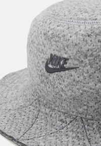 Grauer Bucket-Hut aus strukturiertem Stoff mit einer runden Krone und einem breiten, nach unten geneigten Schirm. Enthält ein gesticktes Nike-Logo.