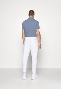 Camisa polo gris con ribetes blancos, combinada con pantalones jogger blancos con puños elásticos. El calzado son zapatillas deportivas blancas.