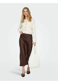 Cardigan crema con bottoni, gonna a pois marroni, borsa bianca tessurizzata e scarpe borgogna a punta. Attenzione ai colori e ai pattern contrastanti.