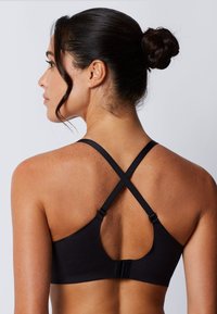 Top deportivo negro con un diseño de espalda nadadora, tela suave, tirantes ajustables y cierre de gancho. Textura lisa con detalles mínimos.