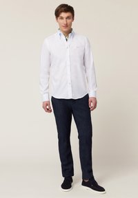 Chemise blanche à manches longues avec un accent de col bleu, associée à un pantalon slim en denim bleu foncé et des chaussures noires à lacets.