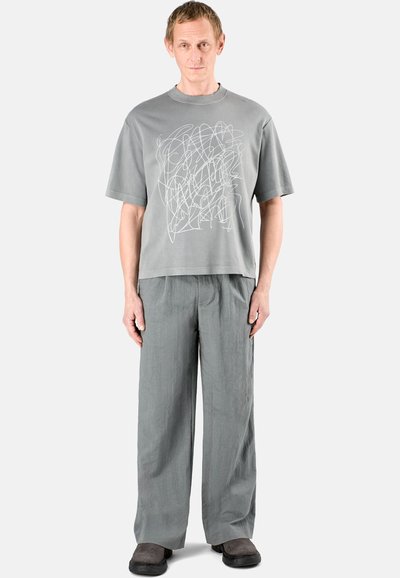 Grå t-shirt med kort ärm och abstrakt vitt linjemönster, kombinerad med löst sittande grå byxor och mörkgrå slip-on skor.