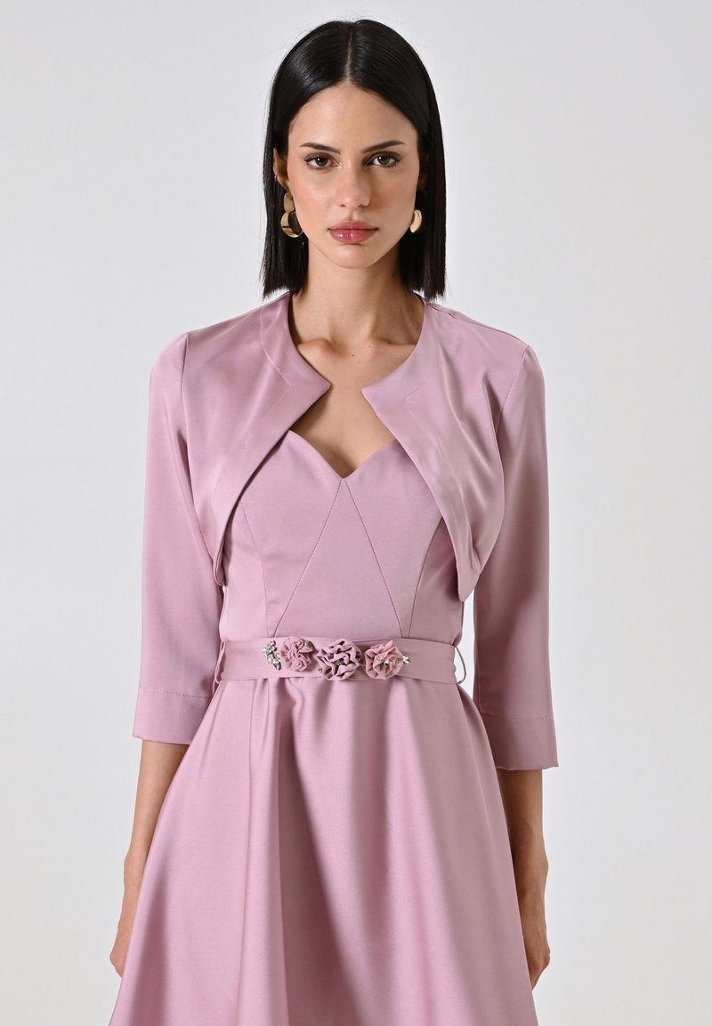 Abito rosa chiaro con corpino aderente e gonna svasata, caratterizzato da un collo a V e maniche a tre quarti, adornato con dettagli floreali in vita.