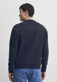 Marineblå hettegenser med rund hals og ribbestrikkede mansjetter. Har en glatt tekstur og en avslappet passform; parret med lyseblå denimjeans.