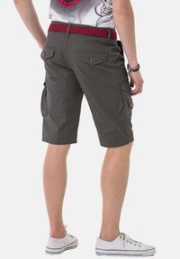 Khaki cargoshorts met een gestructureerde rode en zwarte geweven riem, voorzien van zijzakken en knoopzakken op de achterkant. Strak ontwerp en veelzijdige stijl.