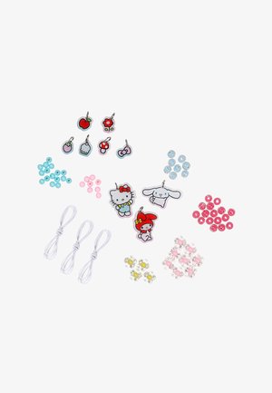 Breloques personnages et fruits, perles colorées, perles en forme de fleur et cordons élastiques blancs disposés sur un fond blanc pour la fabrication de bijoux.