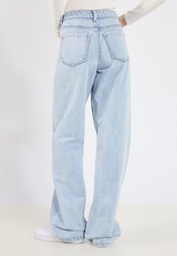 Jean en denim bleu clair, taille haute, à coupe décontractée et jambes larges. Caractérisé par deux poches arrière et une texture légèrement délavée.