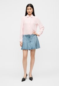 Ανοιχτό ροζ πουκάμισο με κουμπιά και μακριά μανίκια, συνδυασμένο με μπλε τζιν φούστα με πιέτες, ολοκληρωμένο με μαύρες γόβες μυτερές.
