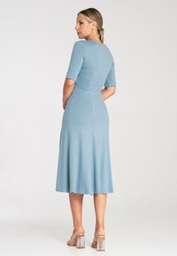 Bla dresses in knieum Länge mit kurzen Ärmeln. Glatte Textur und tailliert, mit sanft auslaufendem Saum. Kombiniert mit klaren Blockabsatzsandalen.