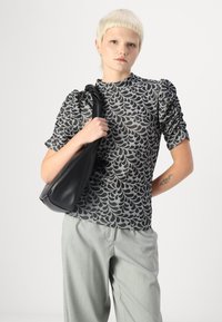 Top preto e cinza com padrão de folhas e mangas bufantes, combinado com calças cinza-claro e uma bolsa preta de ombro. Textura suave no geral.