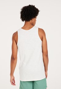 Witte, mouwloze tanktop met een relaxte pasvorm en ronde hals; zachte textuur met een subtiel patroon, gedetailleerde stiksels langs de randen.