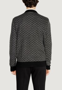 Maglione a righe nero e bianco con colletto e polsini a coste, dotato di una vita attillata e di un motivo testurizzato su tutta la superficie.